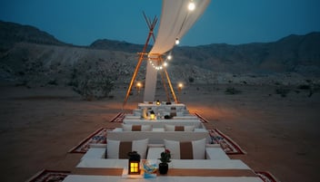 Luxury Ramadan desert Iftar setup in Dubai with lantern-lit dining table under the evening sky in Mleiha dunes.